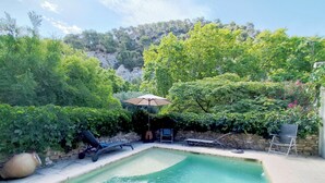 A swimming pool with lounge chairs and an umbrella, surrounded by lush greenery and a stone wall. - Gîte le chat vert. The most beautiful villages in France  (Robion)