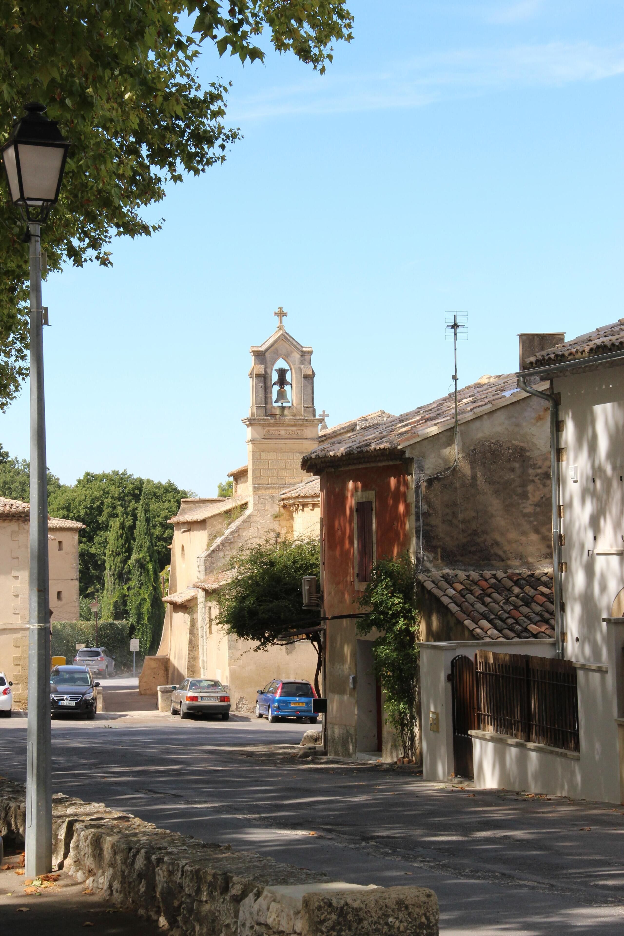 A street with a church in the background, stone buildings, and parked cars.