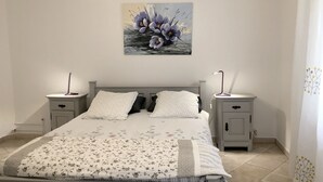 A bedroom with a bed, two bedside tables, a wall-mounted lamp, and a painting of flowers. - Gîte le chat vert. The most beautiful villages in France  (Robion)
