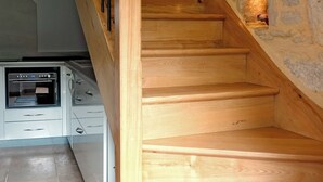 A wooden staircase with stone walls and a kitchen area with white cabinets and an oven.