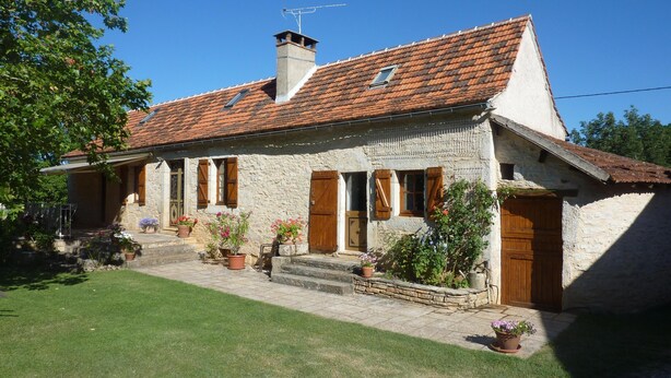 A stone house with a tiled roof, wooden shutters, and a small garden with potted plants.