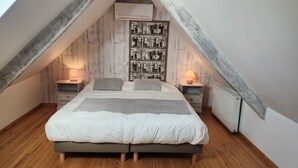A bedroom with a sloped ceiling, wooden walls, a bed with white bedding, two bedside tables with lamps, and a radiator.