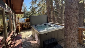 A wooden deck with a hot tub, wooden chairs, and a large tree.