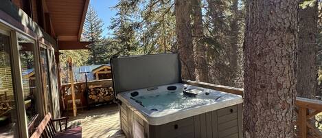 A wooden deck with a hot tub, wooden chairs, and a large tree.