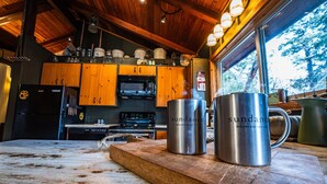 A rustic kitchen with wooden cabinets, a black refrigerator, stainless steel appliances, and two stainless steel mugs labeled 'sundance'.