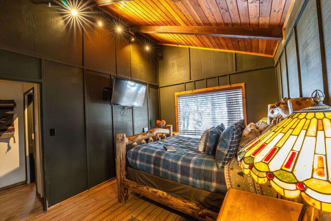 A cozy room with a wooden bed, a television, and a window with blinds.