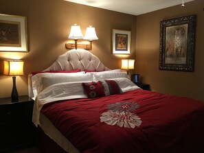 A neatly made bed with a red and white bedspread, two wall-mounted lamps, and framed artwork on the walls.