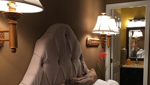 Ett sovrum med en stor säng, två vägglampor, en spegel och en dörr som leder till ett badrum.