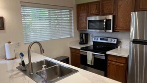 A kitchen with a stainless steel sink, a microwave, an oven, and a refrigerator. - 1 bedroom condo, kitchen, lanai, Princeville (Princeville)