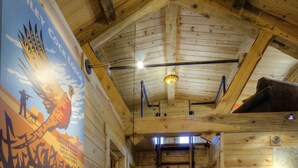 A wooden interior with a ladder leading to a loft area, a poster on the wall, and a wooden floor. - Beautiful Timber Frame Canyon with Spring Creek Canyon views! (Rapid City)