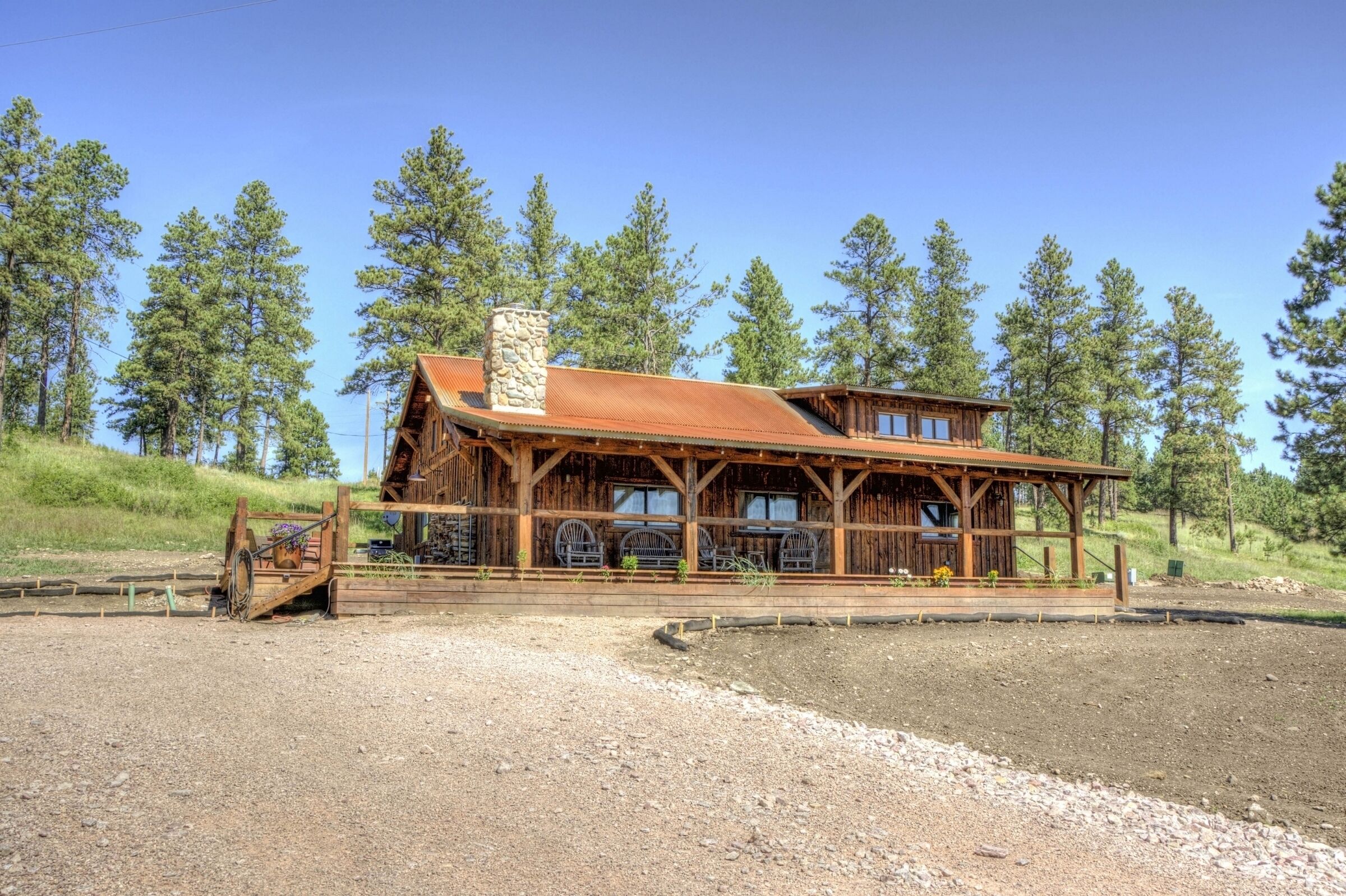 Eine rustikale Holzhütte mit einem Steinkamin, großen Fenstern und einer Veranda mit Sitzgelegenheit im Freien.