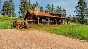 A rustic log cabin with a stone chimney, wooden porch, and a gravel driveway. - Beautiful Timber Frame Canyon with Spring Creek Canyon views! (Rapid City)