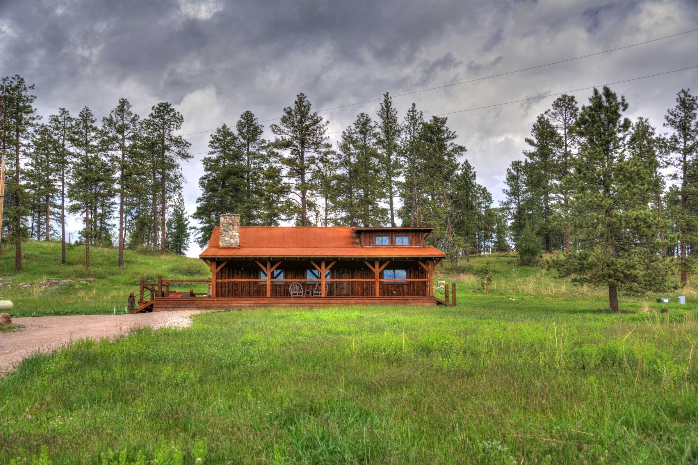 Eine Holzhütte mit Veranda, umgeben von einer Wiese und hohen Kiefern.