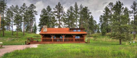 Eine Holzhütte mit Veranda, umgeben von einer Wiese und hohen Kiefern.