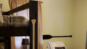 A dormitory room with bunk beds, a lamp, and a window with curtains.