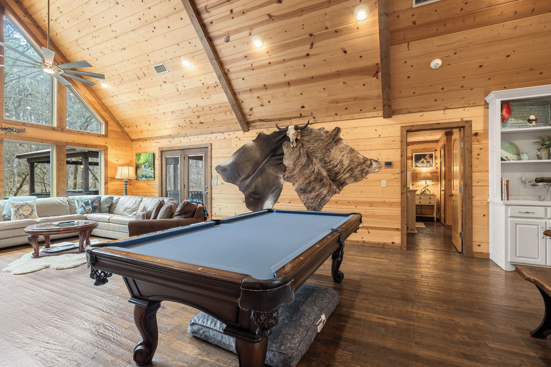 A cozy room with a pool table, wooden ceiling, and large windows.