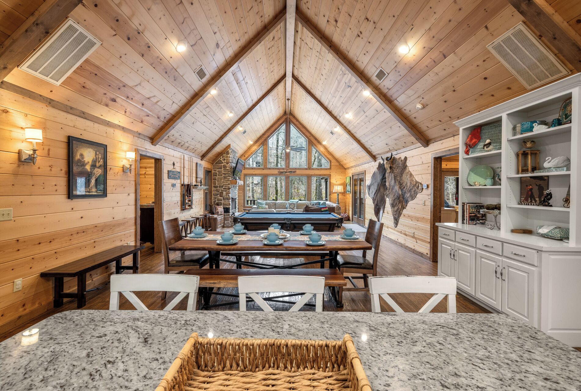 Interior acogedor de una cabaña con comedor, cocina y una gran chimenea de piedra.