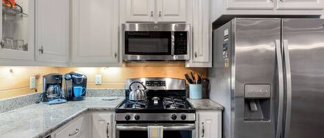 A kitchen with white cabinets, a stainless steel stove, a microwave, and a refrigerator.