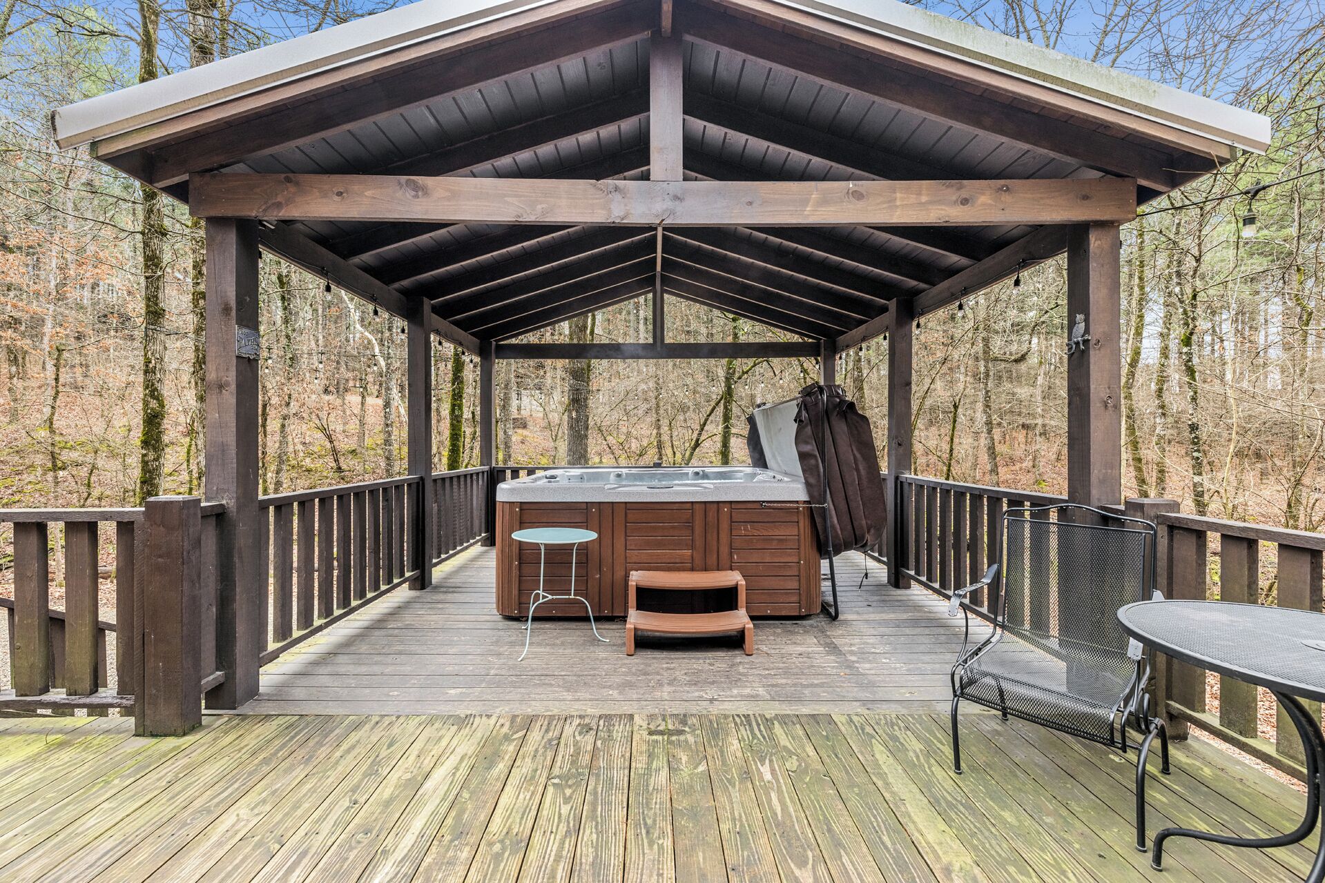 A wooden deck with a hot tub, a table, and a bench.