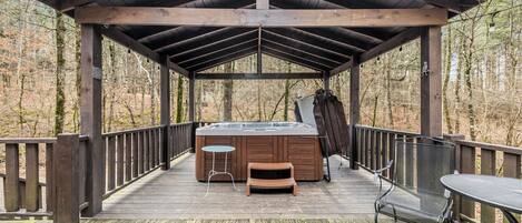 A wooden deck with a hot tub, a table, and a bench.