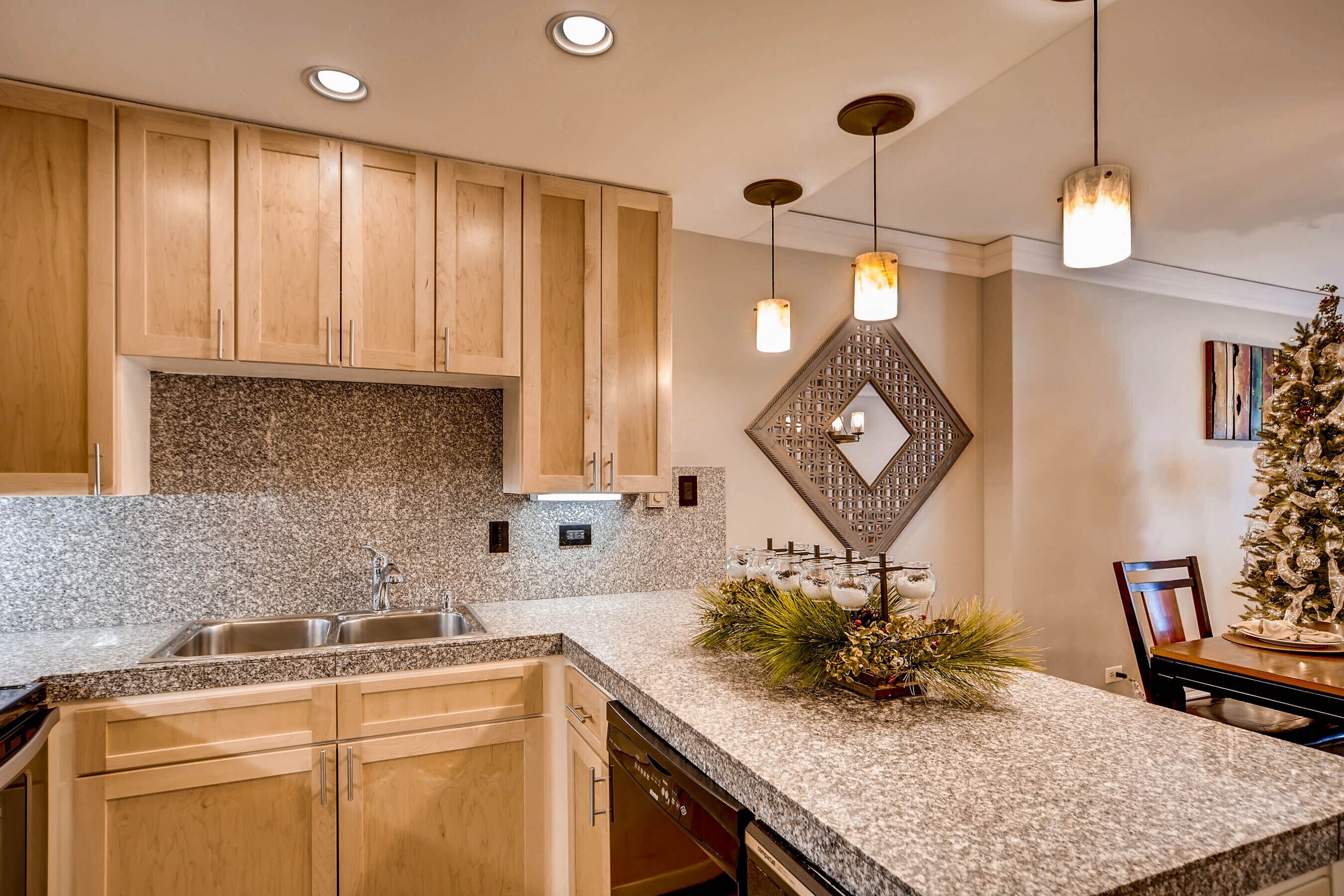 Cocina con encimeras de granito, gabinetes de madera e iluminación colgante.