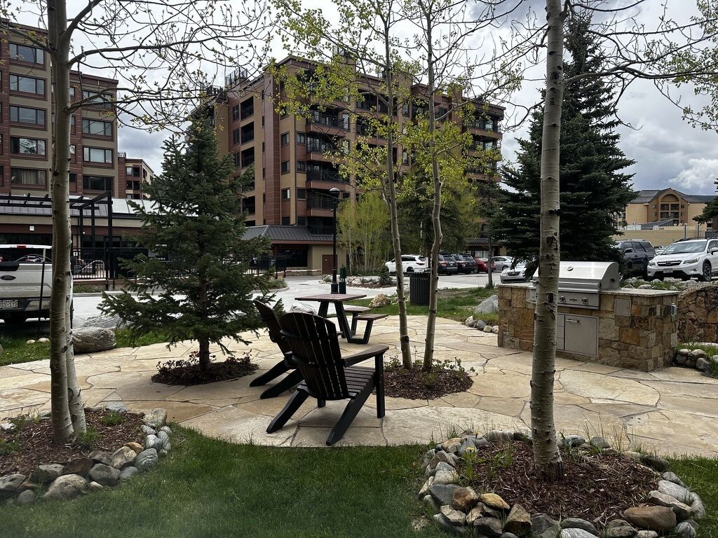 Un patio al aire libre con una mesa y sillas, rodeado de árboles y un muro de piedra.