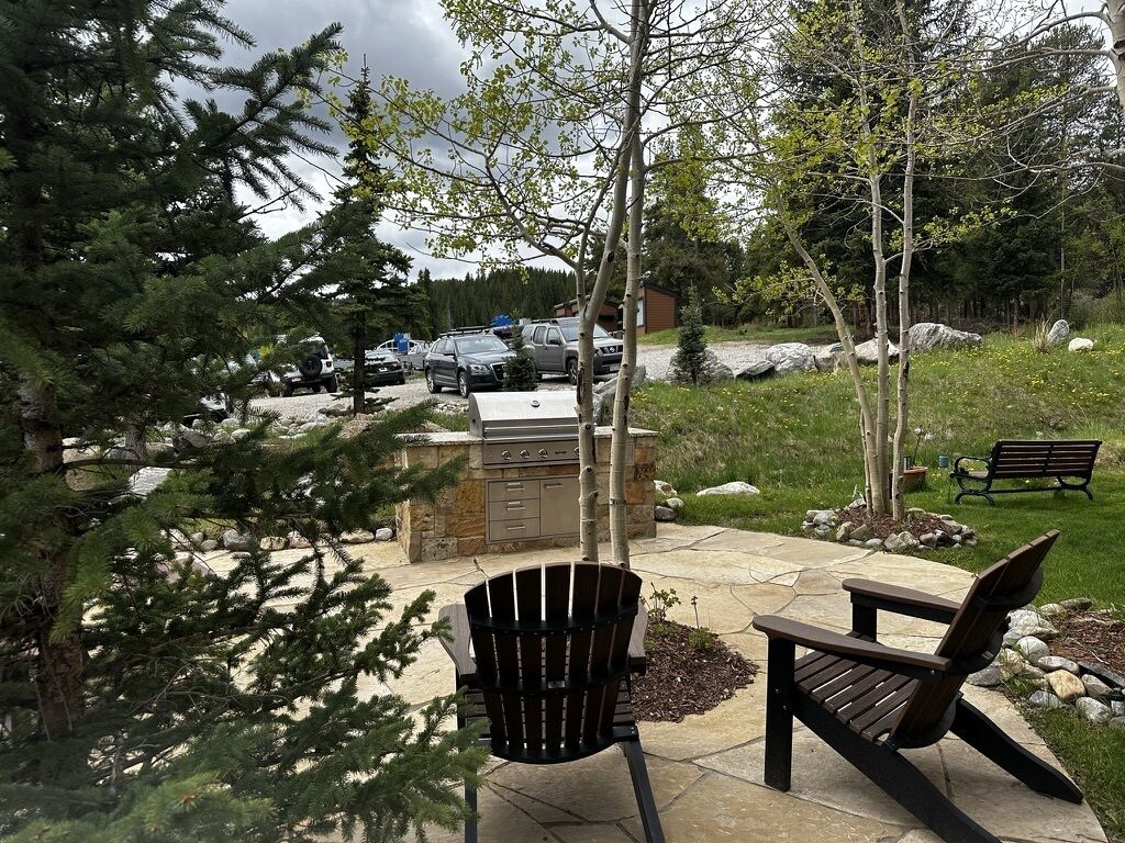 An outdoor patio with a grill, two Adirondack chairs, and a stone pathway.