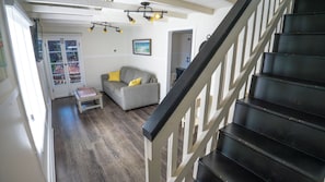 A staircase leading to a landing with a grey sofa and a small table, wooden flooring, and a door with glass panels. - Yellow Beach House 500' to the Waves- Electric Car Charger! (Laguna Beach)