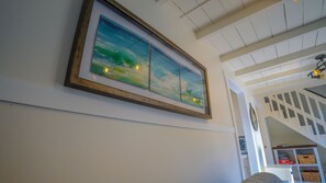 A framed landscape painting on a white wall, a staircase with a white railing, and a ceiling with exposed beams and recessed lighting. - Yellow Beach House 500' to the Waves- Electric Car Charger! (Laguna Beach)