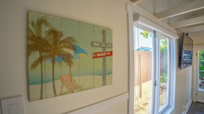 Eine Wand mit einem Strandgemälde, einem Hinweisschild und einer Schiebetür zu einem Außenbereich.