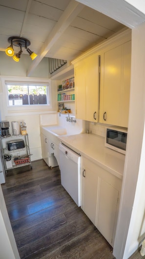 A kitchen with a white countertop, a built-in oven, and a window with a view of a wooden fence. - Yellow Beach House 500' to the Waves- Electric Car Charger! (Laguna Beach)