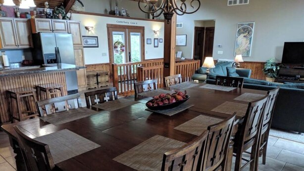 A spacious dining area with a large wooden table, multiple chairs, and a central fruit bowl. - Splendid Home Away From Home -5 Bdr- with Hot Tub (Galena)