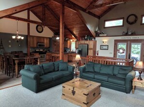 A rustic interior with a high ceiling, wooden beams, a kitchen area, and a seating area with two sofas and a coffee table. - Splendid Home Away From Home -5 Bdr- with Hot Tub (Galena)