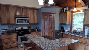 A kitchen with wooden cabinets, granite countertops, a central island, and a microwave. - Splendid Home Away From Home -5 Bdr- with Hot Tub (Galena)