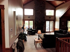 A spacious living room with a stone fireplace, multiple seating areas, and large windows allowing natural light.