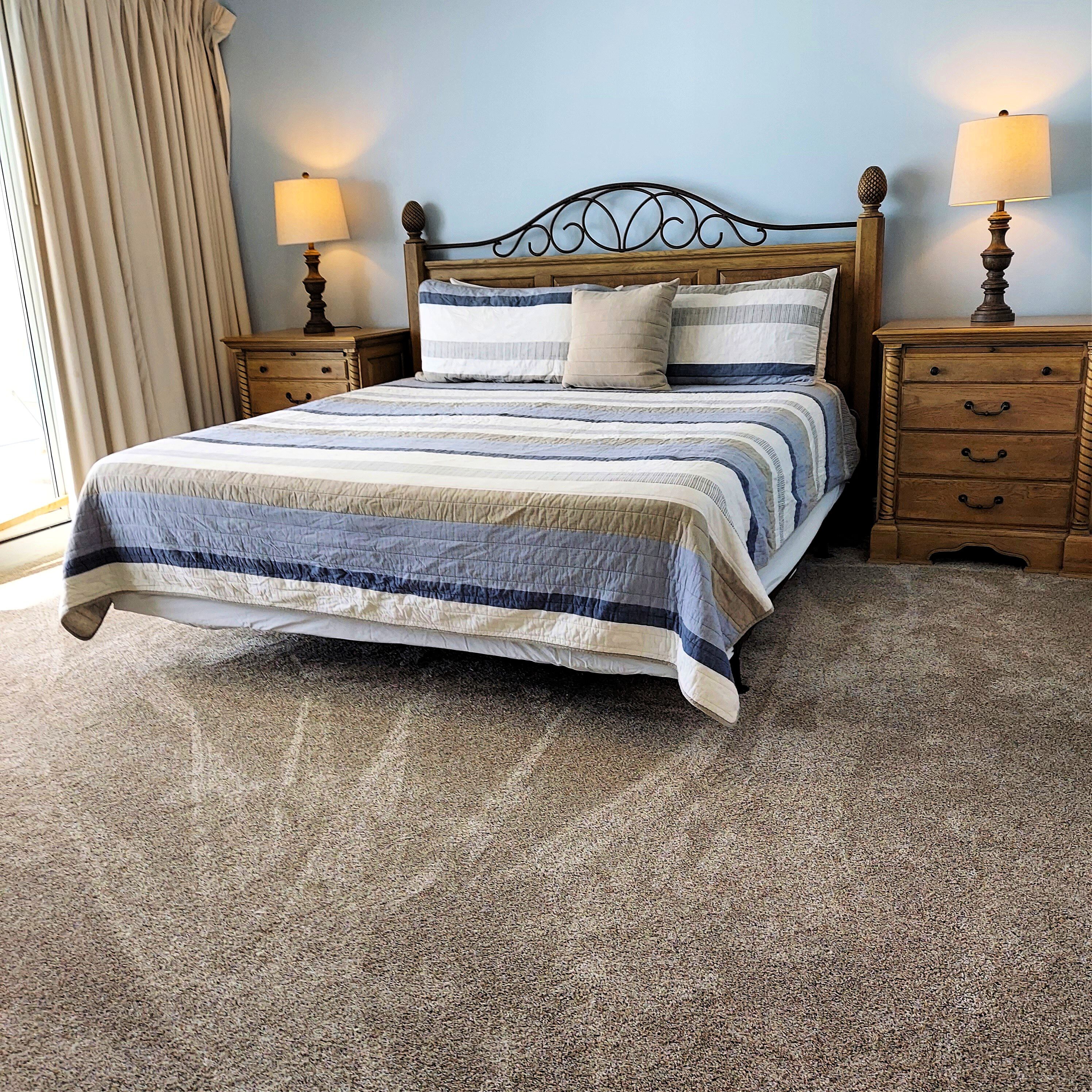 A bedroom with a bed, two nightstands, a wooden headboard, and a beige carpet.