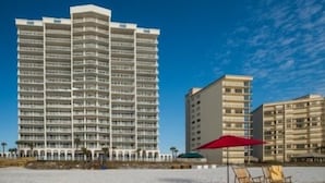 Een hoog hotel met meerdere balkons, gelegen nabij een strand met ligbedden en parasols.
