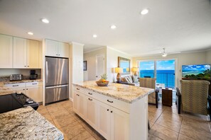 A kitchen with a central island, stainless steel appliances, and a view to the ocean.