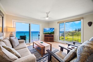 A living room with a sofa, coffee table, and TV, overlooking a balcony with a view of the sea.