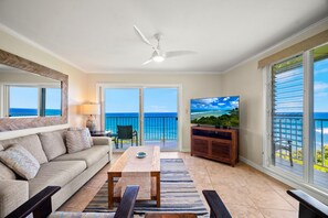 Ein Wohnzimmer mit Sofa, Tisch, Fernseher und einem Balkon mit Meerblick.