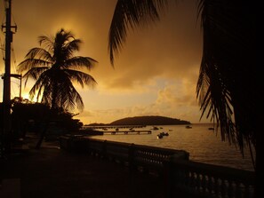 Panorama al tramonto con palme, un pontile e barche sull'acqua.