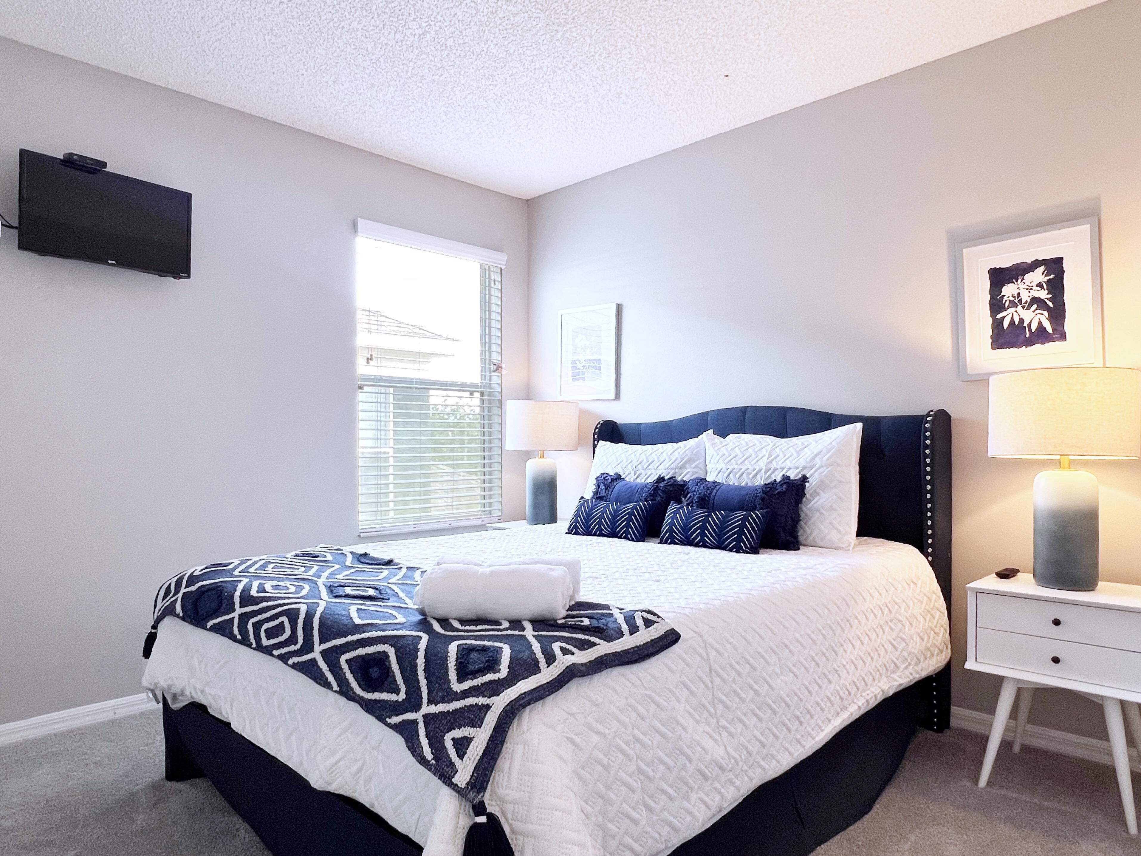 A neatly arranged bedroom with a bed, bedside tables, a TV, and a window.