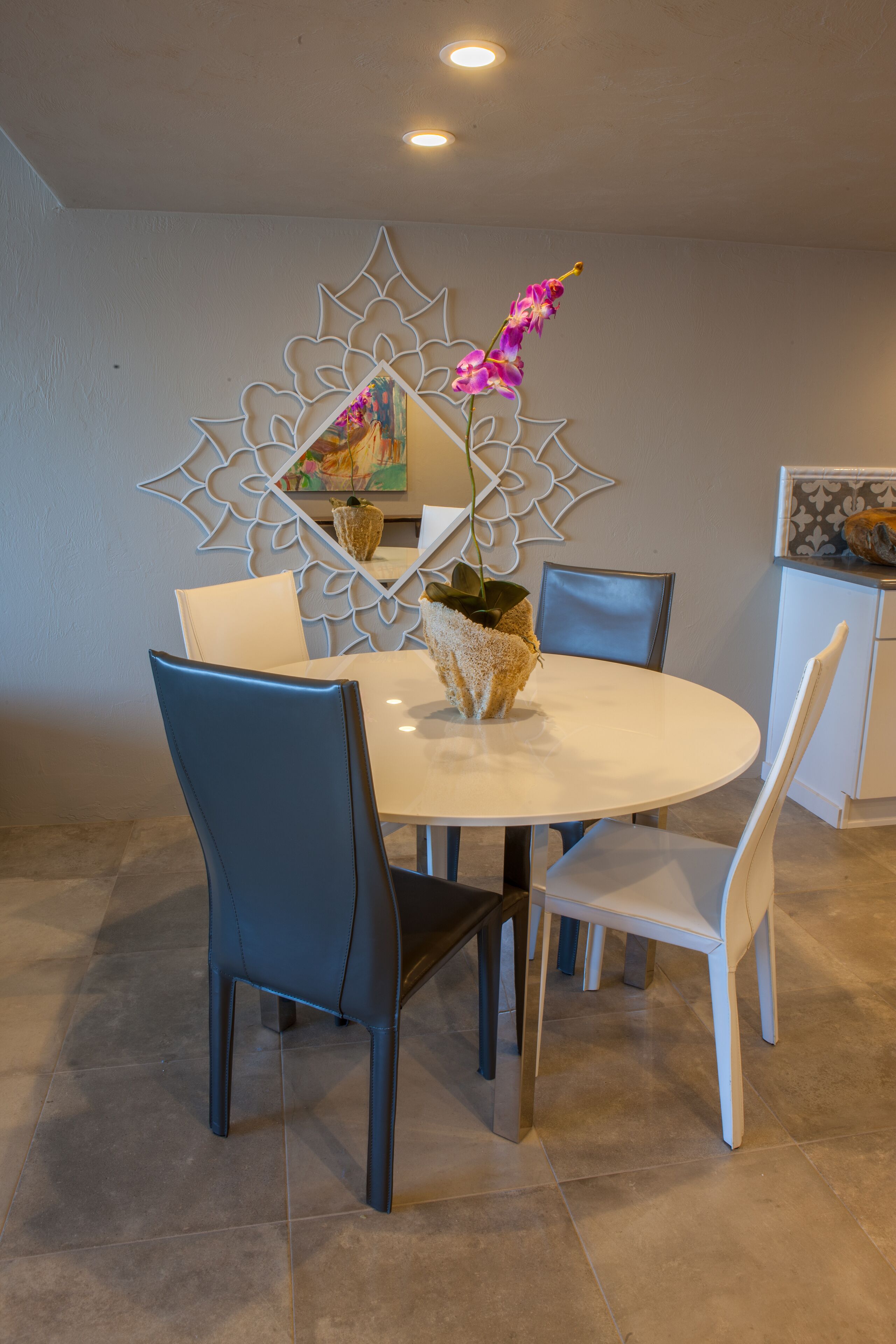 A dining area with a round table, four chairs, a decorative mirror, and a vase with flowers.