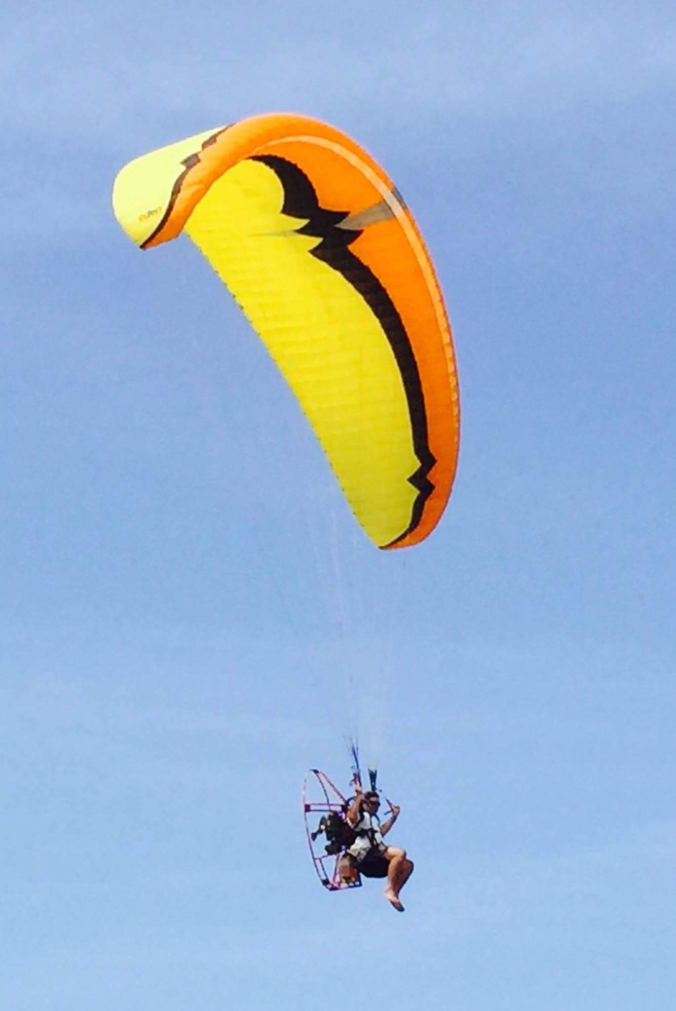 A person paragliding with a large, colorful parachute against a clear blue sky.