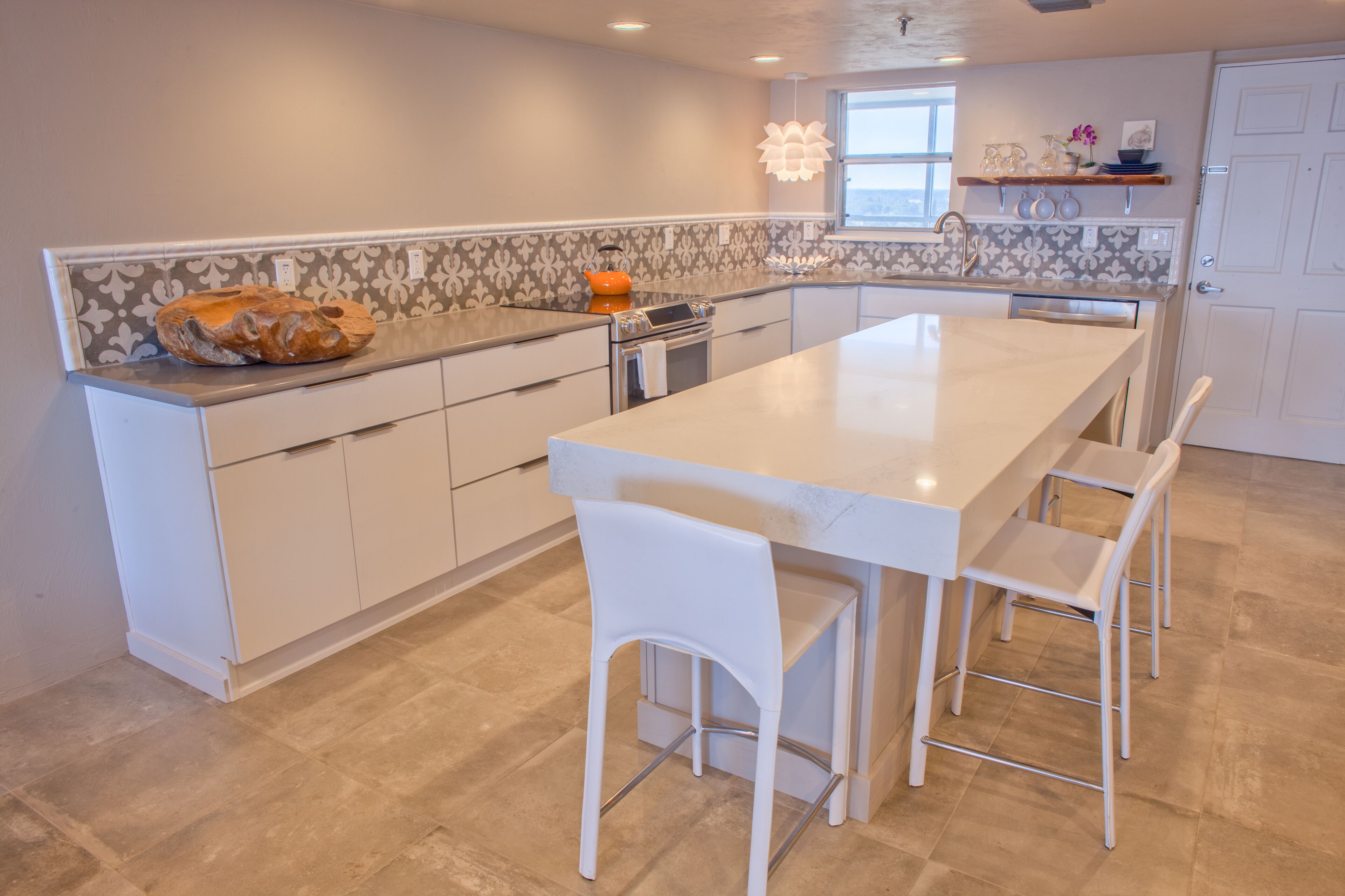 A modern kitchen with a large island, white bar stools, and a decorative vase on the countertop.