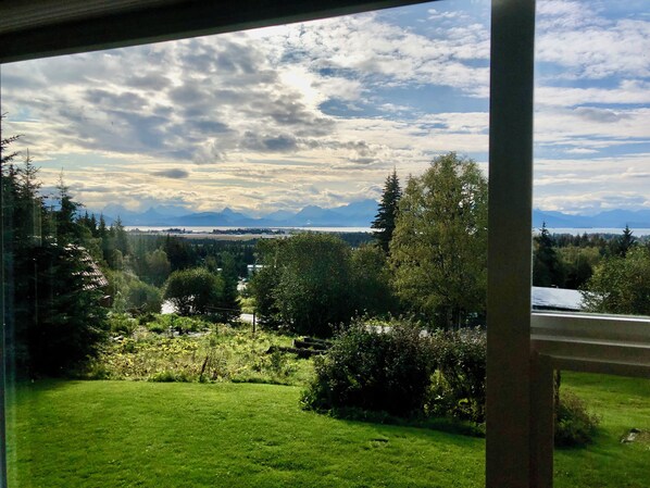 Une vue depuis une fenêtre donnant sur un paysage verdoyant, avec des arbres et une chaîne de montagnes lointaine.