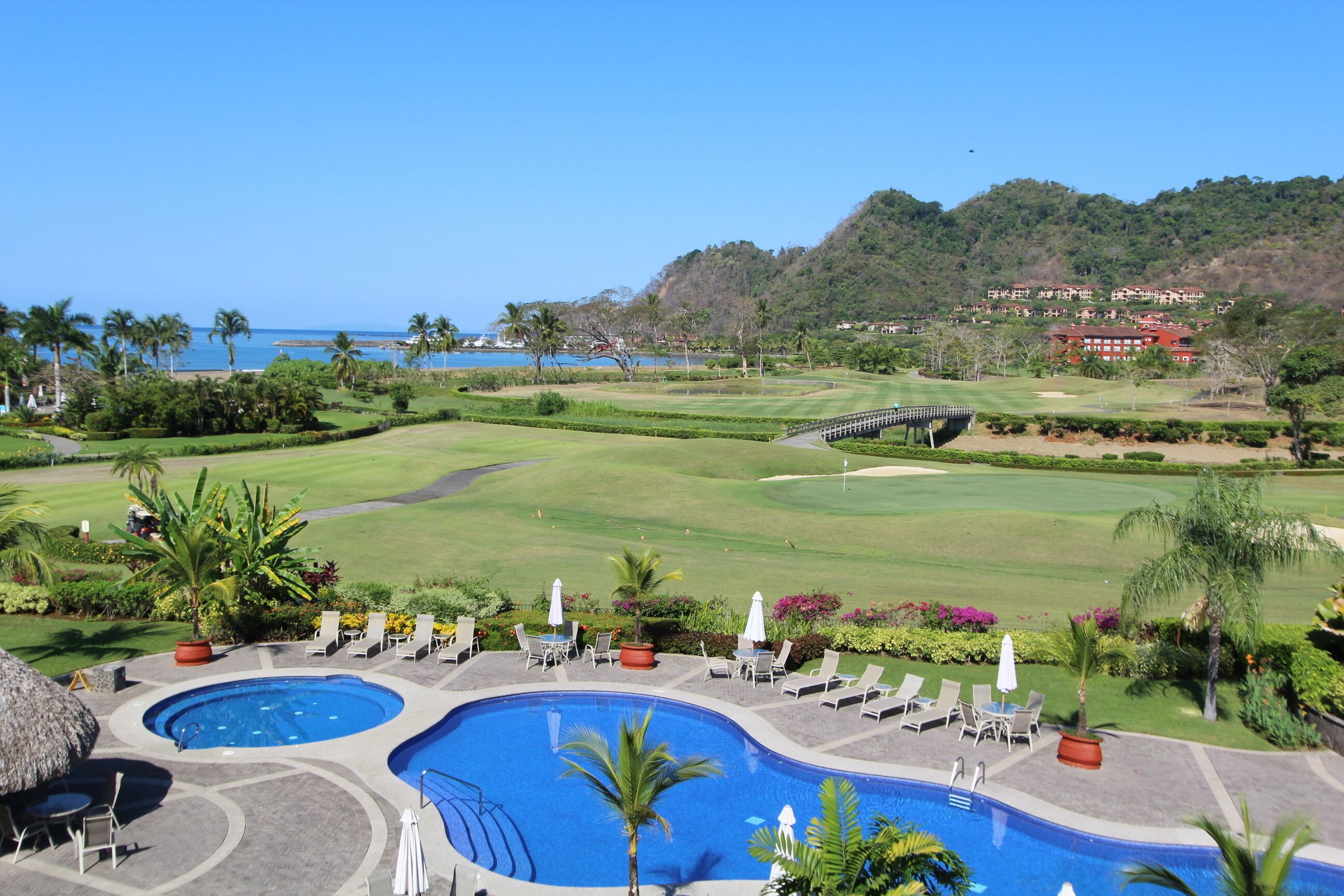 A resort with a large pool area, a golf course, and a view of the ocean.