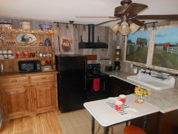 A compact kitchen with wooden cabinets, a black refrigerator, a microwave, a stove, and a window with a view of a red barn. - WELCOME TO THE COUNTRY - LAKE FRONT PROPERTY - THE FOX DEN STUDIO (Red Hook)