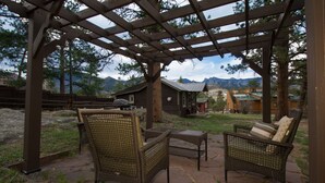 A covered patio with wicker furniture and a view of mountains. - Cozy 2-Cabin Retreat Near RMNP - Estes Park License #3051 (Estes Park)