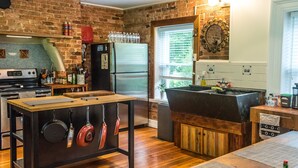 Een keuken met een bakstenen muur, roestvrijstalen apparatuur, een houten tafel en een groot raam.